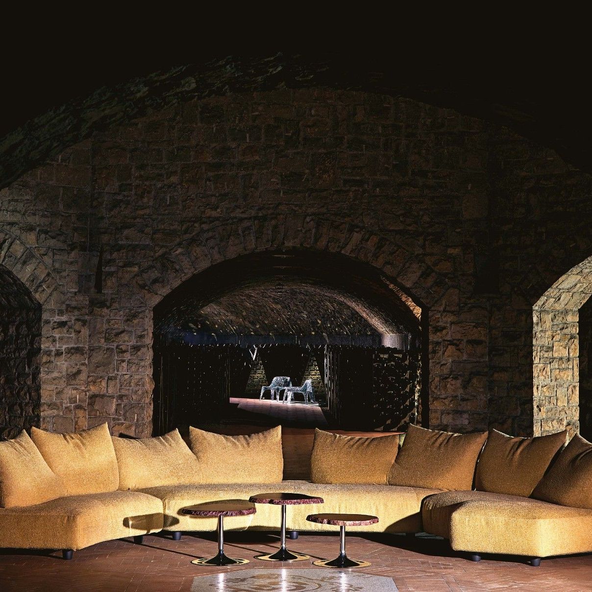  Anywhere, Cicladi, Veronica. Sofas aus Minerals Light Gold und Tische aus bernsteinfarbenem Alabaster unter der Steinkuppel. Im Tunnel der Vintage Collection die Sessel und der Tisch. 
